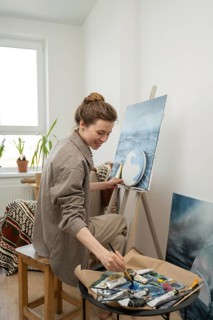 Artist happily working on a landscape painting in a bright, cozy home studio. Paints and brushes