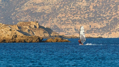 A windsurfer sails near rocks in the blue sea, windsurfer, Meltemi windsurfing spot, Devils Bay,