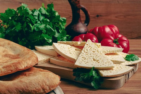 Georgian sliced cheese, on a wooden chopping board, with tomatoes with herbs and lavash, rustic