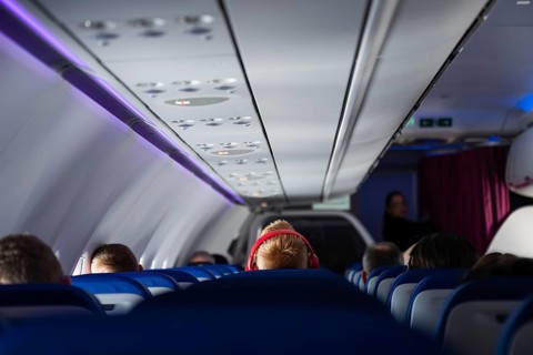 Interior view of a modern airplane cabin with passenger with red headphones seated and blue ambient