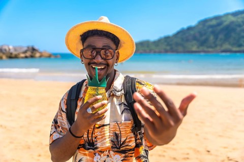 Young black man savoring a refreshing cocktail on a sunny beach, enjoying the vibrant atmosphere