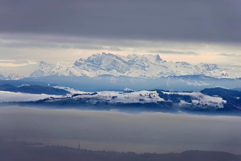 Fog over Lake Zug in the foreground the village of Cham, behind the snow-covered Alps with the