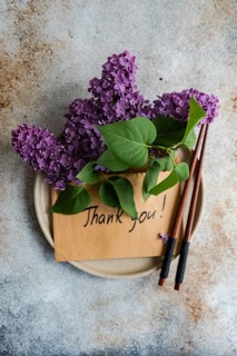 A brown envelope with Thank you written on it, adorned with vibrant lilac flowers and green leaves.
