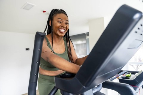 Cheerful black woman enjoys her workout on an elliptical machine during her stay at a hotel,