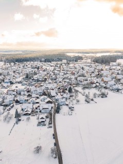 Village in the snow, surrounded by fields under a cloudy sky with sunlight, Calw, Altburg, district