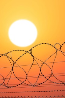 Symbolic image imprisonment, barbed wire fence in front of the sun, sunset, protective fence,