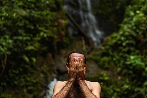 Unrecognizable man covering his face with hands, set against a stunning waterfall in the Choco