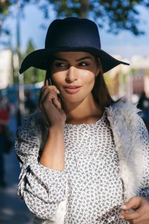 A woman in a patterned dress and navy hat converses on her smartphone, enjoying a sunny day in the
