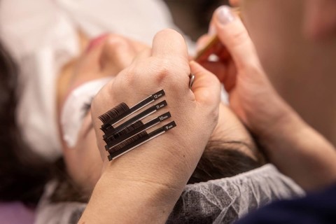 A beauty technician carefully applies eyelash extensions to a client in a salon. Various lash