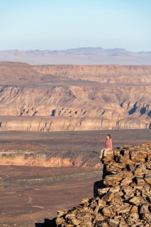 A woman sits on a rock at the edge of the precipice in front of the gorge landscape of the Fish