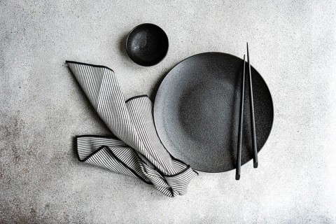 A minimalist black and white table setting with a black plate, striped napkin, and chopsticks