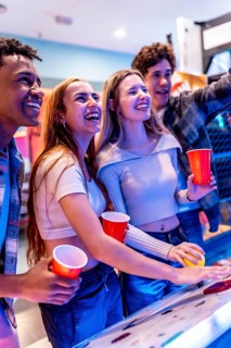 Group of young multiethnic friends laughing and having fun playing arcade games together during a