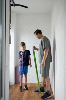 A father and son engage in a fun home workout using resistance bands in a bright room. The duo