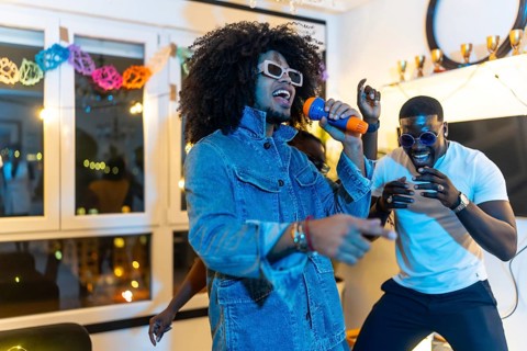 Two latin and african young men singing karaoke in a night home party