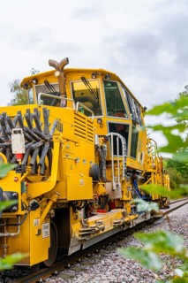 Yellow railway vehicle with technical details and clouds in the sky, tamping machine, Hermann
