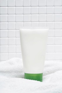 A tube of body care cream on a soft white towel with a tiled bathroom wall in the background,
