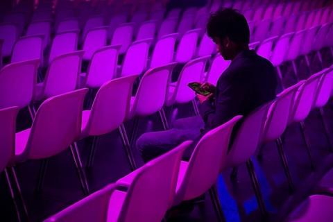 A indian man sits in a purple lit auditorium at a conference of AI in Amsterdam, quietly engaging