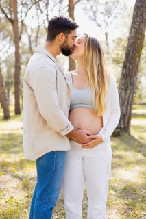 A pregnant woman and her partner share a tender moment outdoors, surrounded by nature's tranquility
