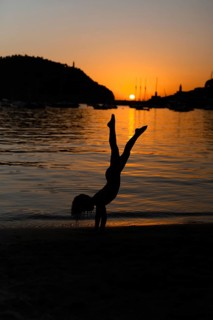 A silhouette of a child doing a handstand on a sandy beach at sunset in Soller, Majorca. The serene