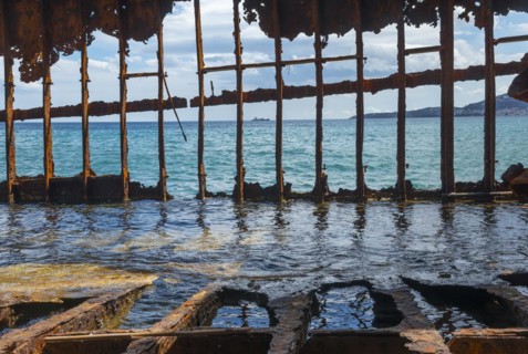 Rusty shipwreck standing half in the water, view through the crumbling structure to the sea,