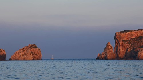 Sunrise over the sea with sailboat and rock formations, morning light, Tsichli Babas islet,