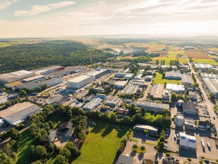 Industrial area with numerous buildings and roads, surrounded by large open fields under a sunny