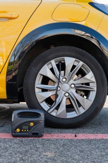 Close-up of an electric car's wheel with a portable tire inflator attached. The yellow vehicle is