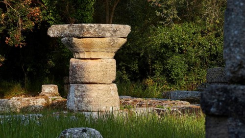 Ancient stone column in shade surrounded by grass and trees, Archaeological Site, Ancient Olympia,