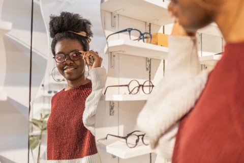Black woman trying on sunglasses in a stylish eyewear store. She is wearing a red and white