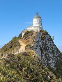 Nugget Point Lighthouse with Nugget Rocks in front of a blue sky, South Island, New Zealand,