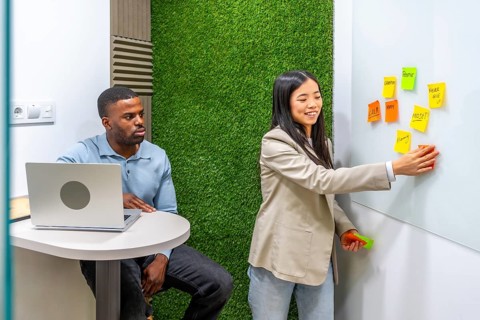 Businesswoman sticking notes on whiteboard during a brainstorming session with her colleague in a