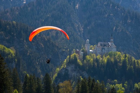 A paraglider flies high above Neuschwanstein Castle in the mountains, Schwangau near Füssen,