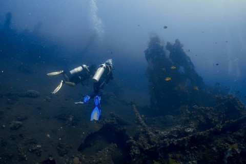 Two divers explore a shipwreck on the seabed in the deep blue surroundings of the ocean, dive site
