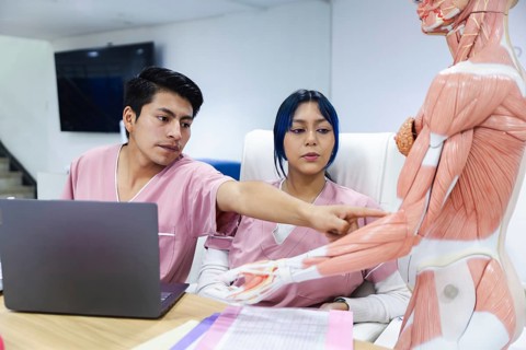Physical therapists in Ecuador study an anatomical model. Dressed in pink, they concentrate