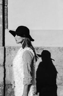 A black and white photo of a stylish woman wearing a black hat and textured vest, casting a