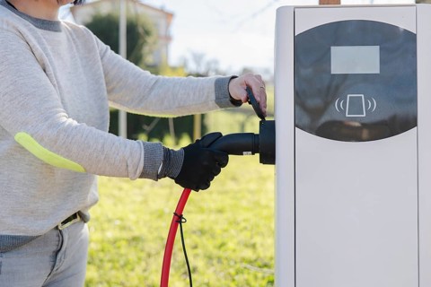 A person is plugging an electric car into a charging station outdoors. The scene highlights