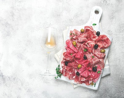 Assorted, meat appetizer, prosciutto, salami and ham, with olives, on a wooden white board, light