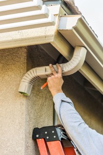 Worker Attaching Aluminum Rain Gutter and Down Spout to Fascia of House