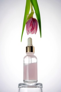 A graceful tulip hangs above a glass cosmetic with a dropper, containing a pink liquid. This