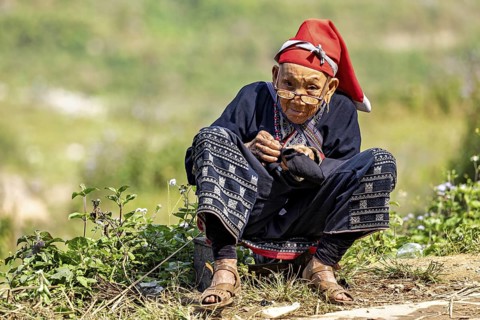 Woman in traditional dress sitting outdoors and doing handicrafts, Large Buddha statue at Fansipan