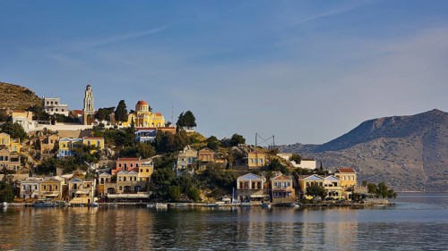 View of a Greek coastal town with colourful houses and a church surrounded by mountains, Symi Town,