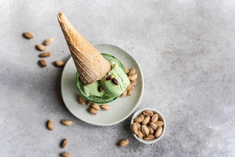 A scoop of pistachio ice cream on a plate, topped with a waffle cone and surrounded by scattered