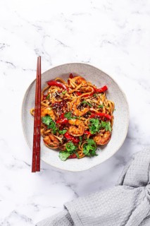 Udon noodles, shrimp with vegetables and fresh herbs, in a bowl with chopsticks, light background,