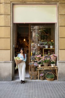 A woman stands at the entrance of a charming flower shop, holding a vibrant bouquet. Blooming
