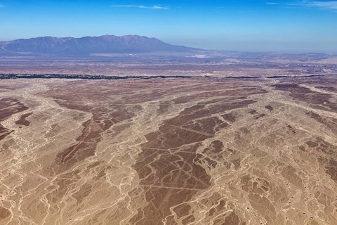 Aerial view of a vast, dry desert with mountains on the horizon under clear blue sky, The landscape
