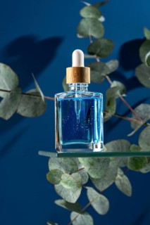 A blue cooling face serum for men, presented in a clear glass dropper bottle, elegantly surrounded