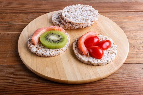Rice cakes with salmon, kiwi and cherry tomatoes on wooden background. close up