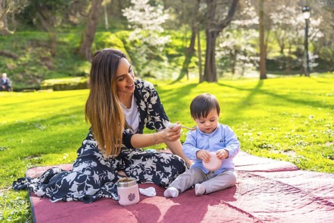 Young mother feeds her baby during a picnic in a park on a beautiful sunny day, enjoying quality