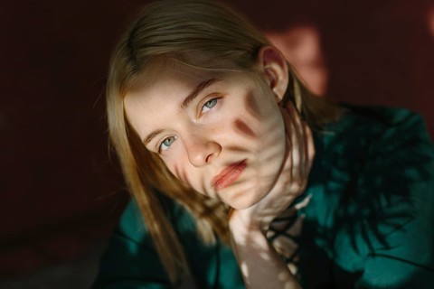 A thoughtful teenager poses outdoors, with sunlight casting artistic shadows across their face. The
