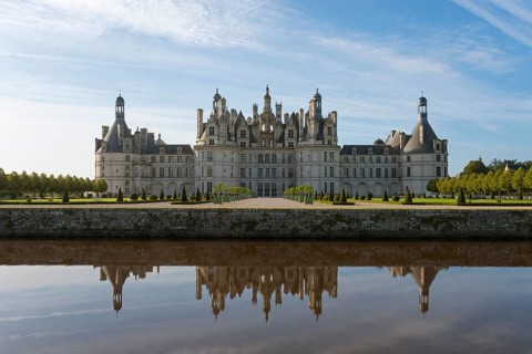 Impressive castle building with towers and windows, reflected in the calm water of the canal, under